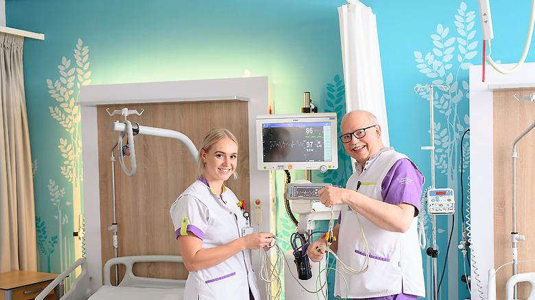  Verpleegkundigen van de Acute Opname Afdeling Jasmijn Hop en Henk Huizing staan samen in een patiëntenkamer bij het apparatuur